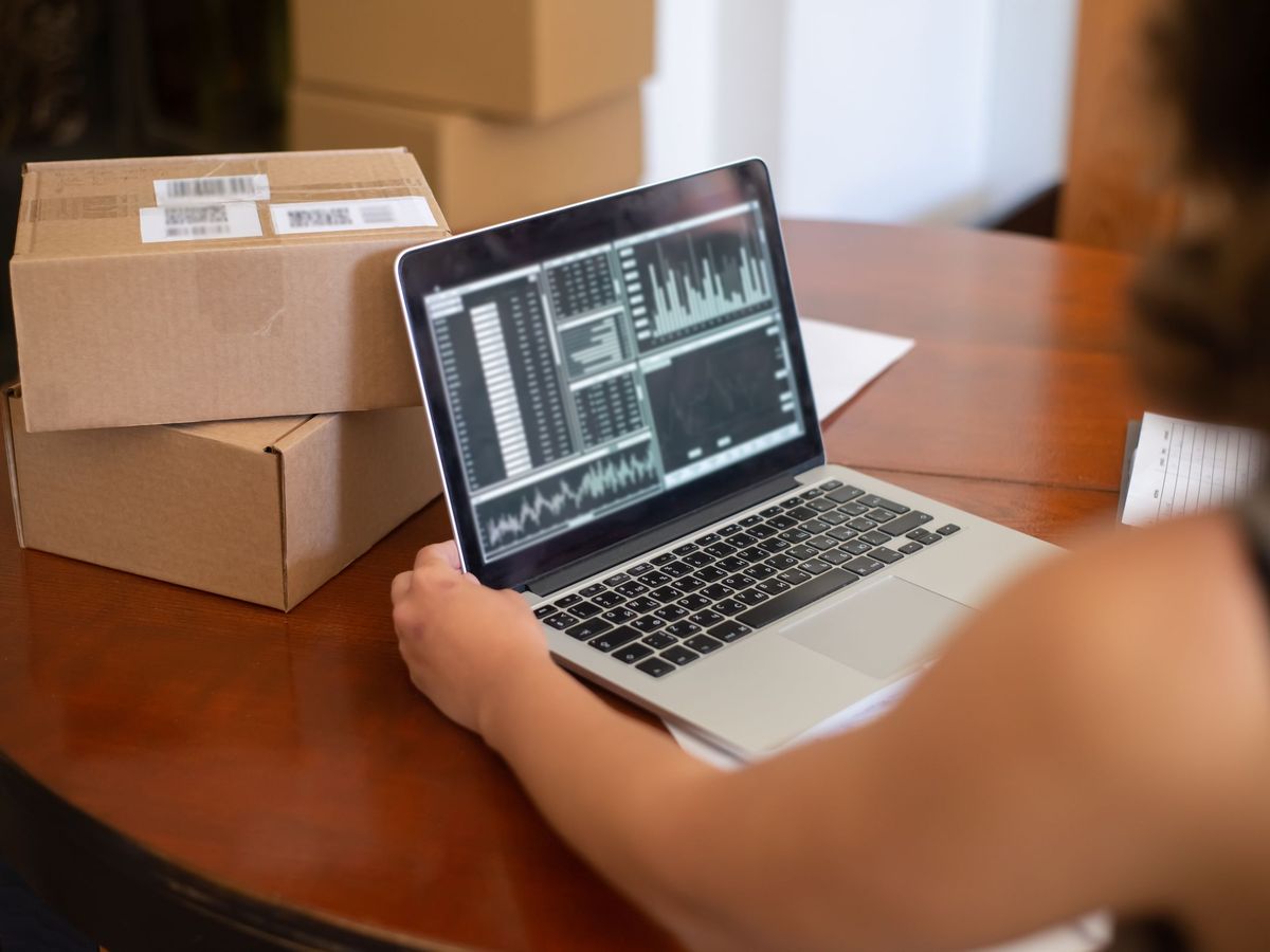 A small business owner checking charts on a laptop next to stacked shipping boxes